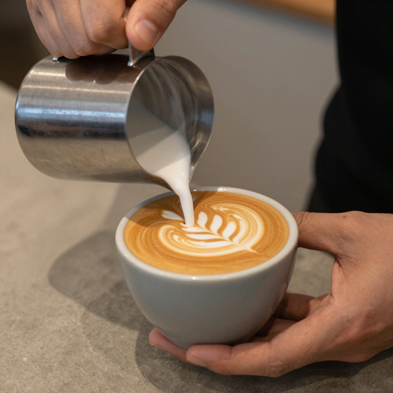 Barista pouring latte art into a ceramic coffee cup, warm lighting, wood counter